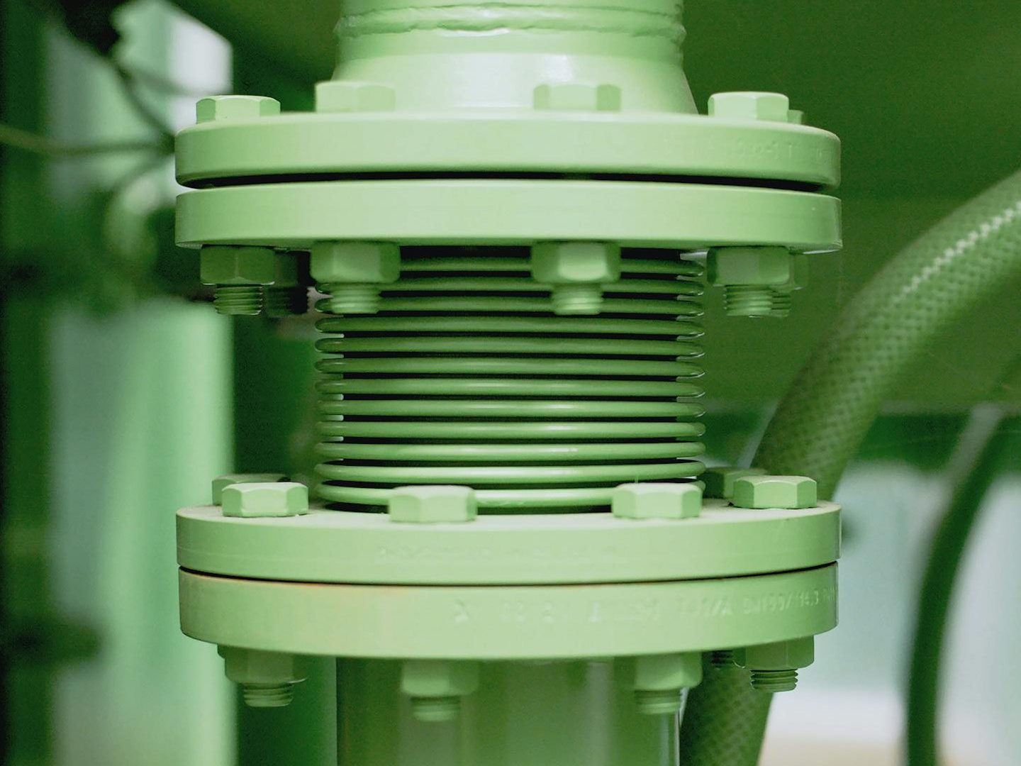 Detailed view of a green industrial pipe and valve system in a mechanical setting.